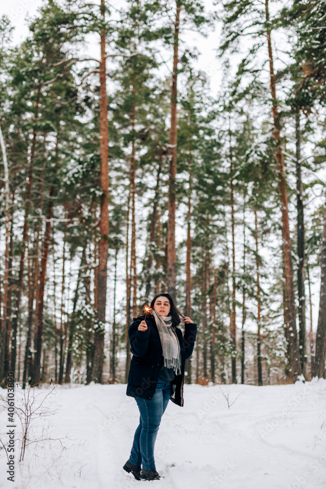 Adult young woman with sparklers on the background of winter pine forest