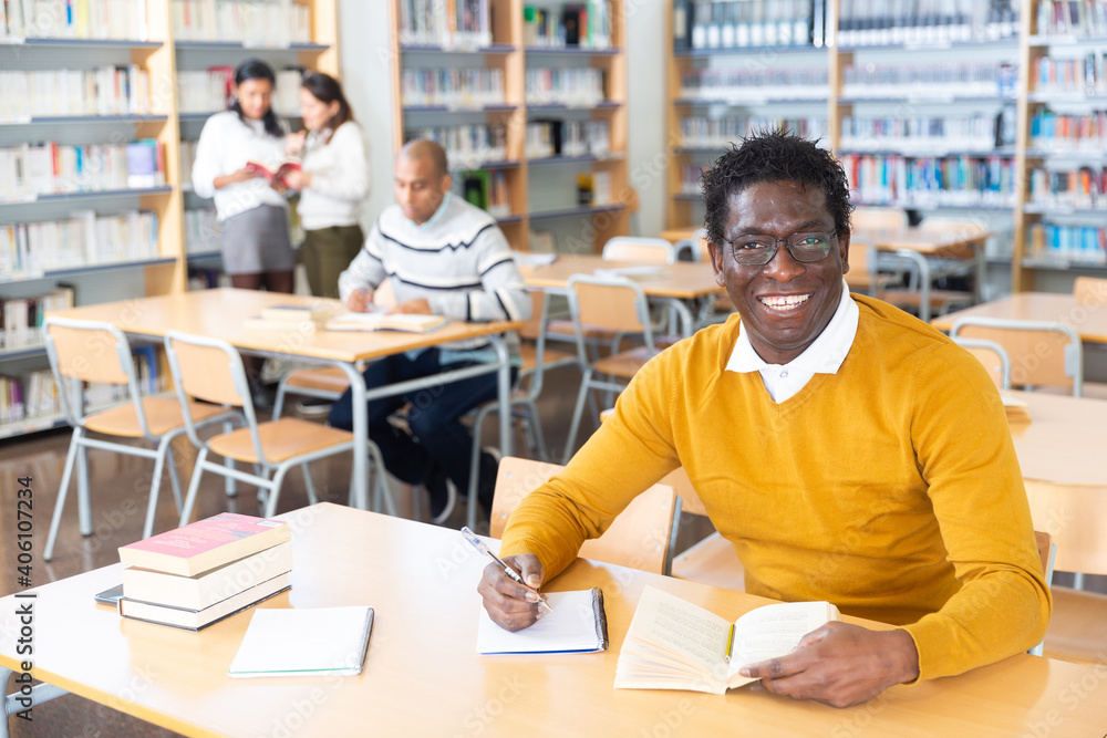 Portrait of confident young adult man studying in at public library