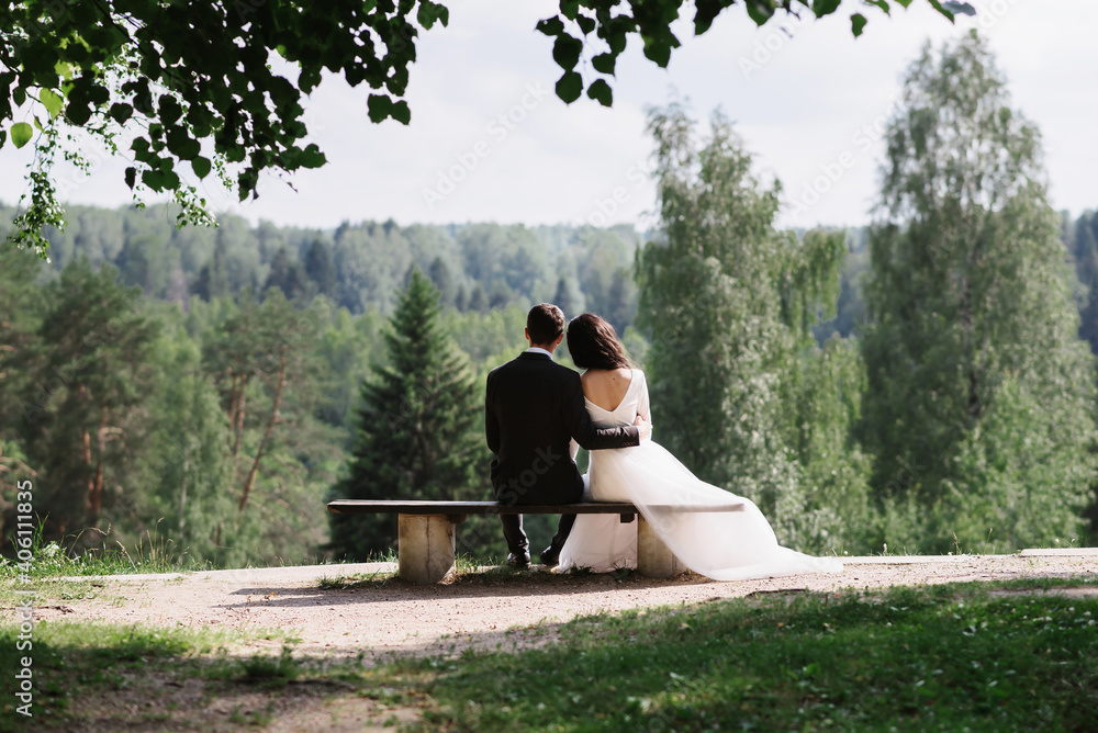 couple bride and groom embrace sitting on a bench on a wedding day in summer