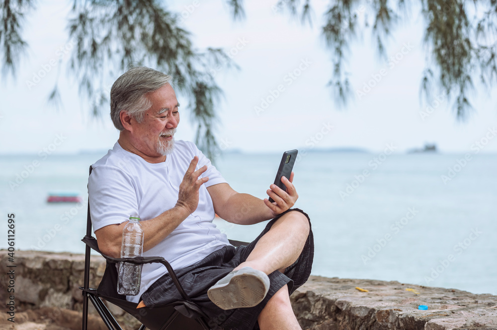 senior elder take vdo call with mobile, he is very happy and smile in outdoor background.