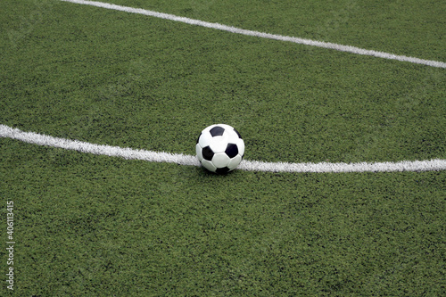 White and black ball for playing soccer lays on green synthetic grass near center of sport playground