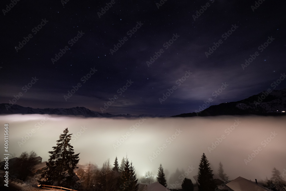 The mist rising over the swiss alps village of La Tzoumaz, in the background the swiss alps against starry sky.