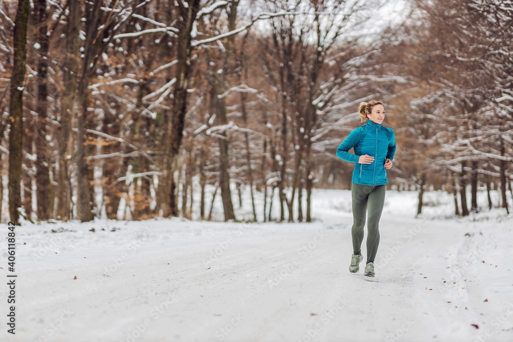 Fit sportswoman running in nature on a snowy path. Cold weather, snow, healthy life, fitness Fit sportswoman running in nature on a snowy path. Cold weather, snow, healthy life, fitness