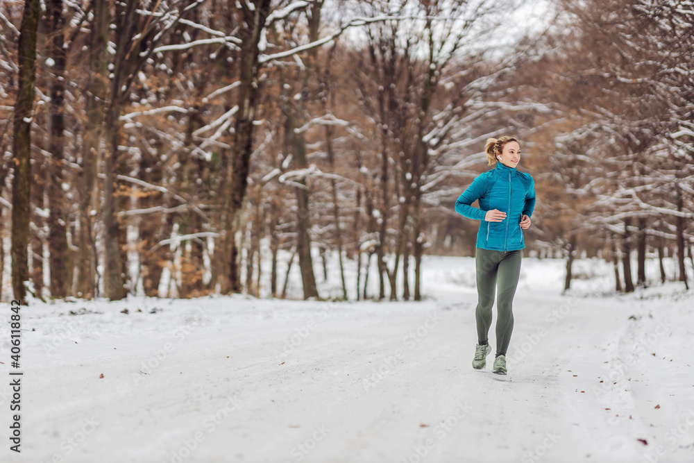 Fit sportswoman running in nature on a snowy path. Cold weather, snow, healthy life, fitness