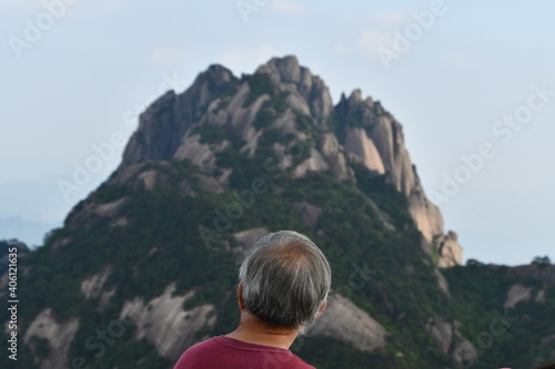 Old chinese man from the back is ovserving monumental pick of Huangshan, China