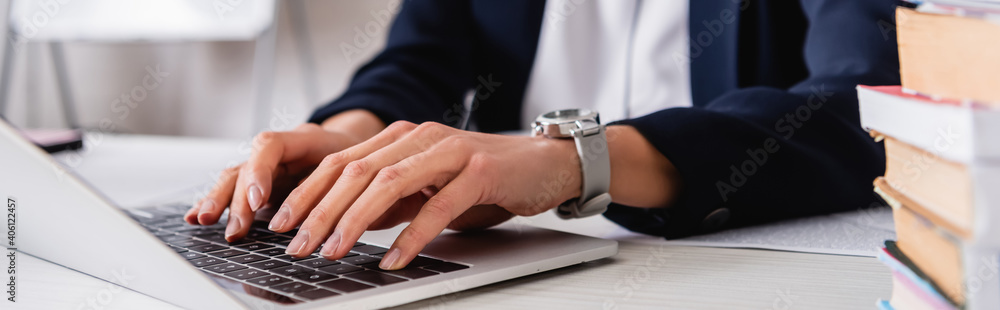 cropped view of interpreter typing on laptop near dictionaries on blurred foreground, banner cropped view of interpreter typing on laptop near dictionaries on blurred foreground, banner