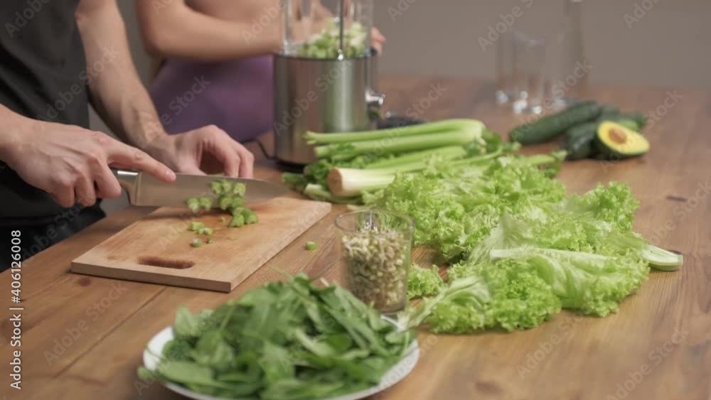 Man cuts the ingredients for making green vegetable smoothies. Woman halpes him. healthy food concept Man cuts the ingredients for making green vegetable smoothies. Woman halpes him. healthy food concept