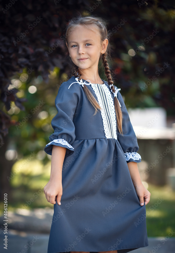 Charming little girl in a retro dress walking in the city on a sunny summer day. Little girl wear school uniform. Primary school girl with long hair. Study and education. Charming little girl in a retro dress walking in the city on a sunny summer day. Little girl wear school uniform. Primary school girl with long hair. Study and education.