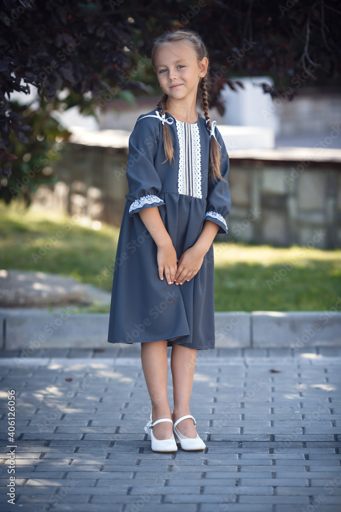 Charming little girl in a retro dress walking in the city on a sunny summer day. Little girl wear school uniform. Primary school girl with long hair. Study and education. Charming little girl in a retro dress walking in the city on a sunny summer day. Little girl wear school uniform. Primary school girl with long hair. Study and education.