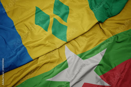 waving colorful flag of myanmar and national flag of saint vincent and the grenadines.