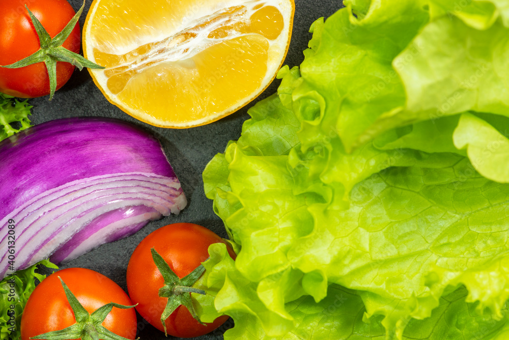 Green lettuce, purple onion, cherry tomatoes, lemon on a dark background. Green lettuce, purple onion, cherry tomatoes, lemon on a dark background.
