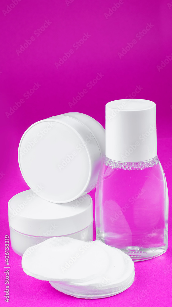 white containers with cosmetics (face cream, hand cream, mineral water, cotton pads) on white pink, arranged vertically white containers with cosmetics (face cream, hand cream, mineral water, cotton pads) on white pink, arranged vertically