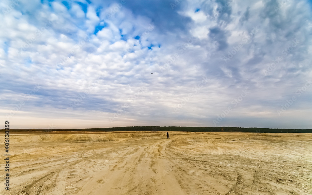 Fototapeta premium Sandy plain and a man in the background against the background of the forest and the blue sky with clouds