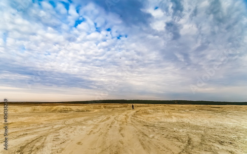 Sandy plain and a man in the background against the background of the forest and the blue sky with clouds
