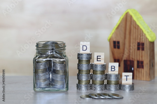 Home loan, Stack of coins money and model house with wooden blocks with the word debt on wooder background, Mortgage debt pressure concept photo