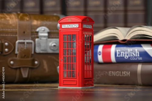 Obraz Learn English concept. Red telephone booth on backgrpund of english course textbook and vintage suitcase.
