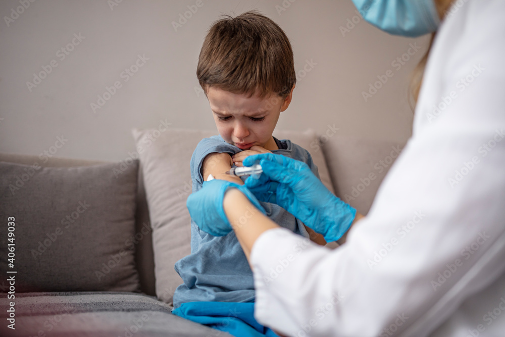Portrait of crying little boy during a Immunization. A kid getting an injection in his arm by a doctor. Little boy getting vaccinated from Covid-19. A young doctot's hand holding a vaccine syringe. Portrait of crying little boy during a Immunization. A kid getting an injection in his arm by a doctor. Little boy getting vaccinated from Covid-19. A young doctot's hand holding a vaccine syringe.