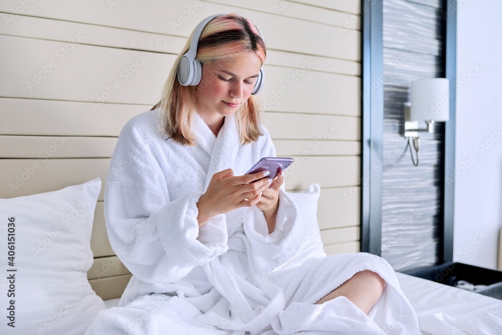 Teenager girl in white bathrobe and headphones with smartphone in her hands Teenager girl in white bathrobe and headphones with smartphone in her hands