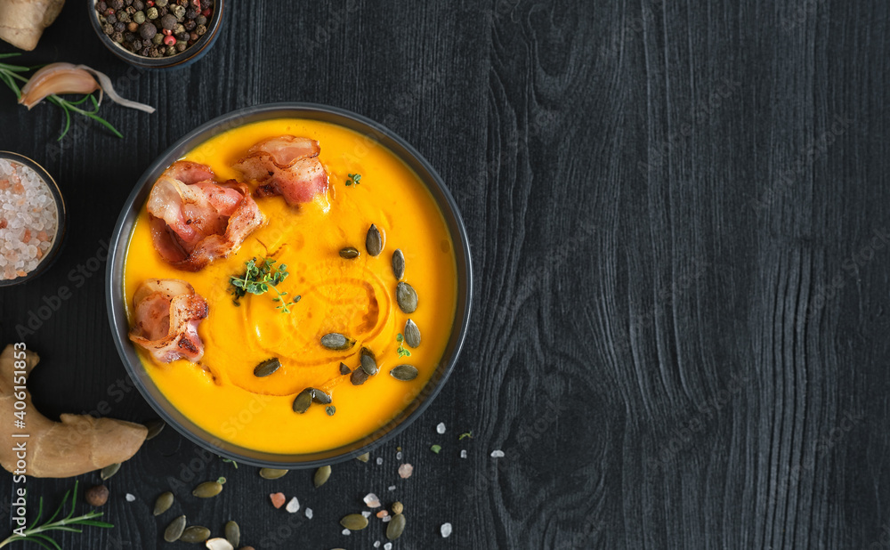 Creamy pumpkin soup with sauteed bacon slices with cream and pumpkin seeds in a black bowl on a black wooden table. Top view with copy space. Ingredients for making pumpkin soup on the table Creamy pumpkin soup with sauteed bacon slices with cream and pumpkin seeds in a black bowl on a black wooden table. Top view with copy space. Ingredients for making pumpkin soup on the table