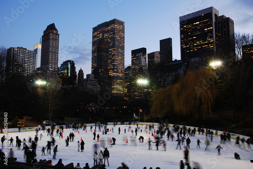 A crowd gathers on the Wollman ice rink under the New York City Skyline