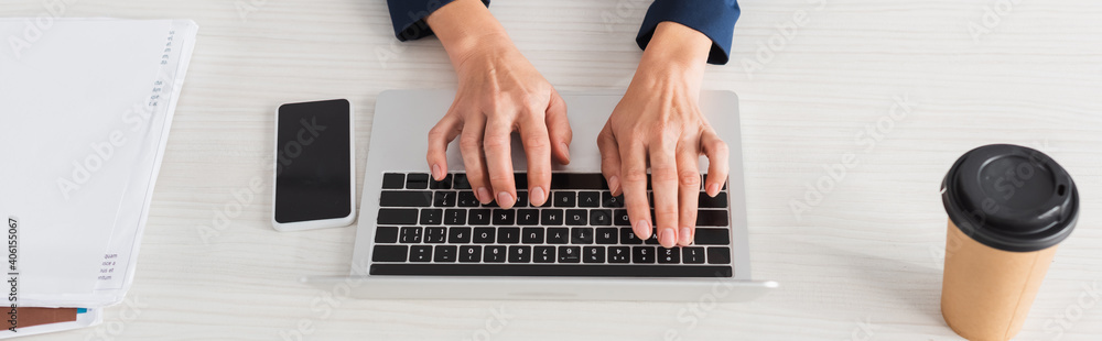 cropped view of team leader typing on laptop keyboard near smartphone with blank screen and coffee to go, banner cropped view of team leader typing on laptop keyboard near smartphone with blank screen and coffee to go, banner