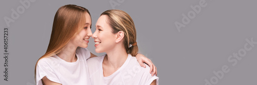 Mother and daughter studio portrait. Grey background. Smiling people. Two female person family. Friends hug. Communication adult. Copyspace. Close noses. Happy woman and girl