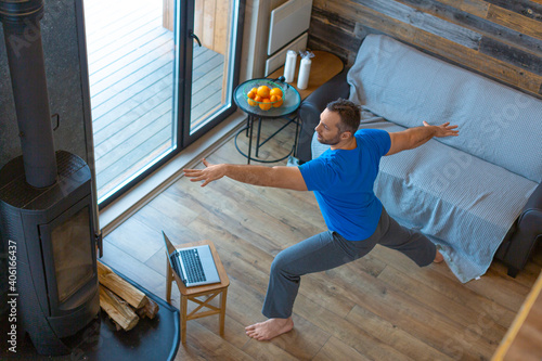 A man is doing yoga at home in front of a laptop monitor.