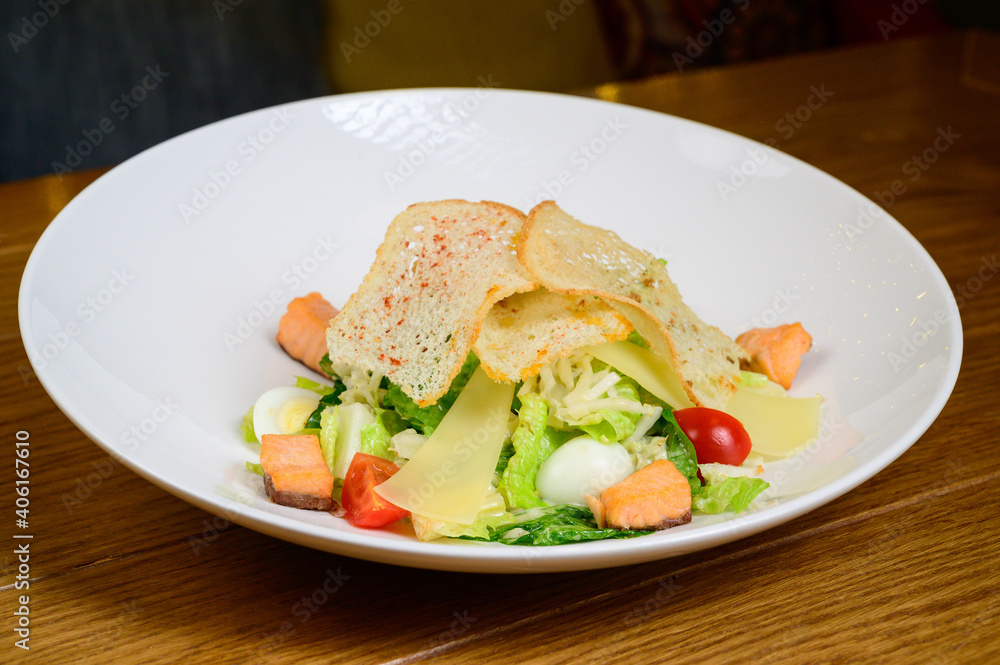 Caesar salad with salmon on white plate on wooden background