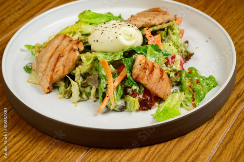 Caesar salad with croutons, quail eggs, cherry tomatoes and grilled chicken in wooden table