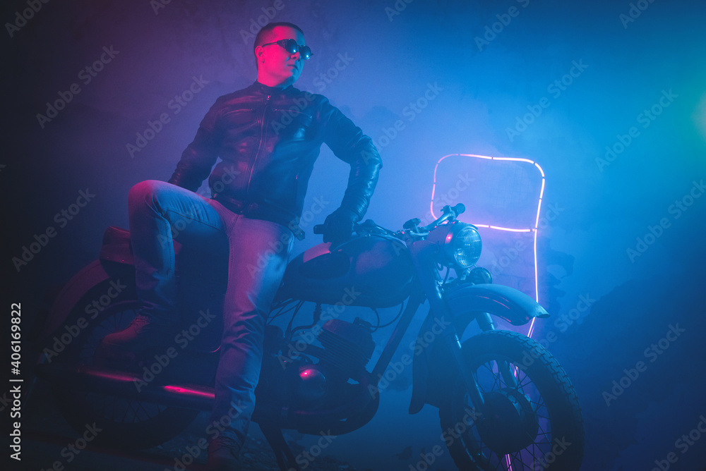 Motor biker in the neon lights on the old brick wall background.