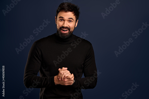 Handsome good-looking stylish caucasian guy in black high neck sweater, rubbing hands and smiling politely, want sale something, making good deal,suggesting buy product, stand Pacific Blue background