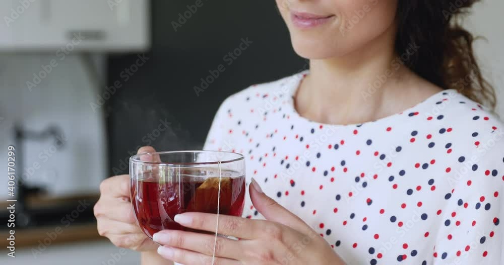 Close up happy peaceful young beautiful woman holding glass cup, drinking herbal tea brewed from sachet, smelling pleasant aroma, enjoying dreamy calm morning time alone at home, planning day. Close up happy peaceful young beautiful woman holding glass cup, drinking herbal tea brewed from sachet, smelling pleasant aroma, enjoying dreamy calm morning time alone at home, planning day.