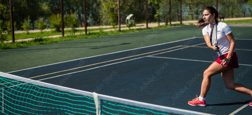 Sportive caucasian woman playing tennis on an outdoor court. Widescreen.