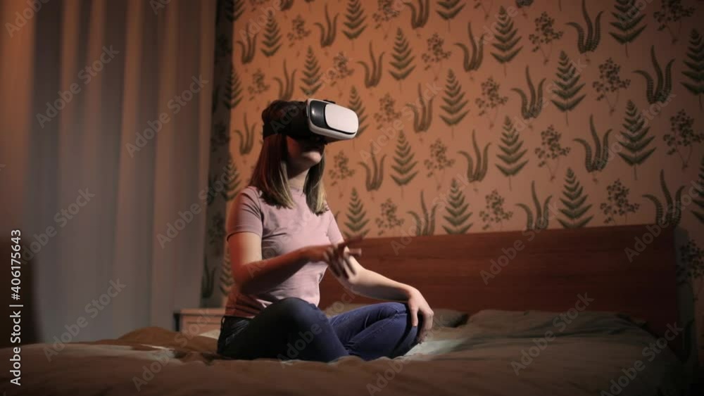 VR technology in education for self-using. Woman sitting in bed in virtual reality 3d glasses and learning something. There's a blinking colourful light all around her. Studying languages or science. VR technology in education for self-using. Woman sitting in bed in virtual reality 3d glasses and learning something. There's a blinking colourful light all around her. Studying languages or science.