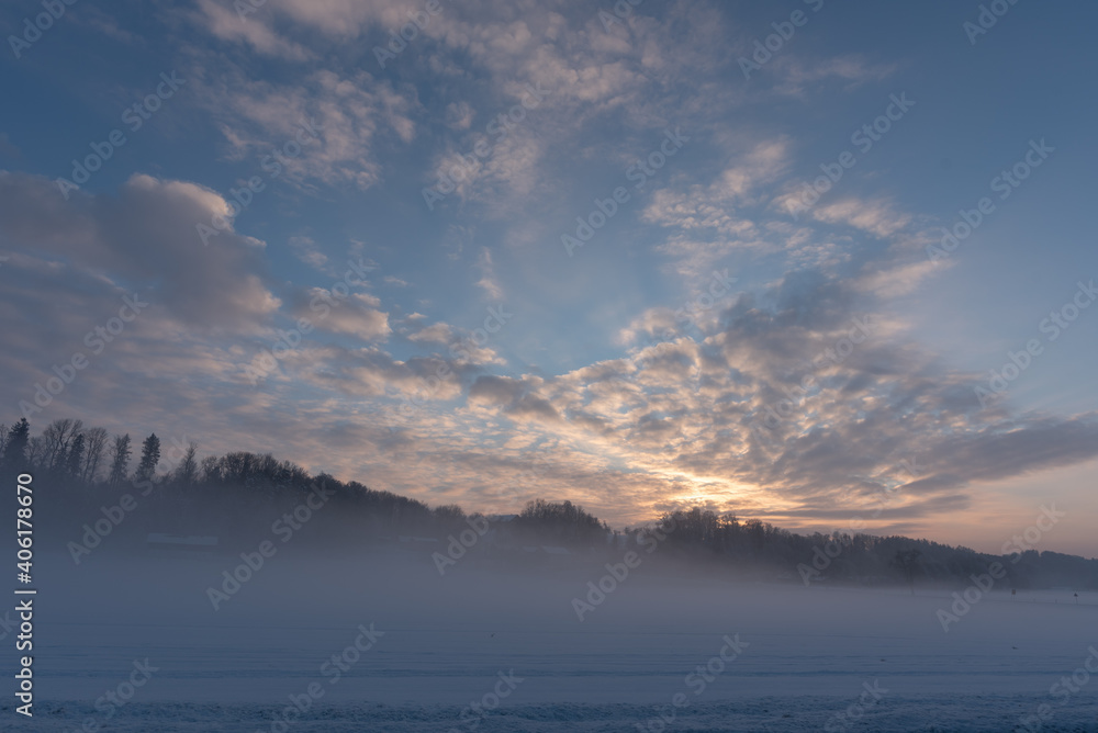 Sonnenuntergang  auf dem Land  b ei Nebel und Schnee im Winter  mit Feld, Wald,  Wolken