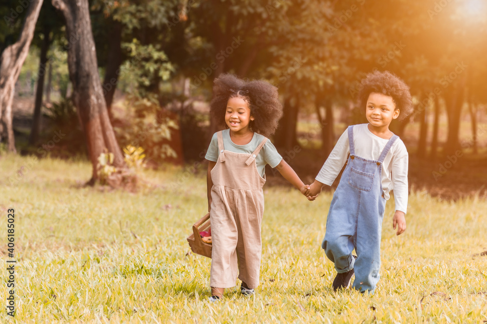 Fototapeta premium Portrait of two adorable african children, girl and boy holding hand and walking together in garden.