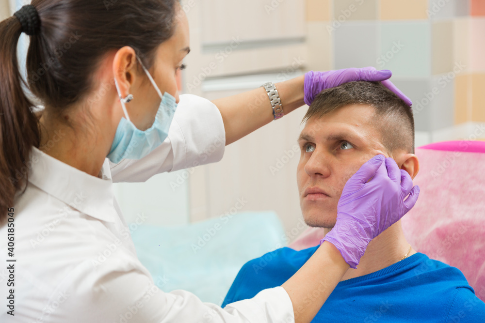 Obraz premium A female doctor stretches the skin on the face of a male patient checking the elasticity of the skin before the rejuvenation procedure in the cosmetic clinic