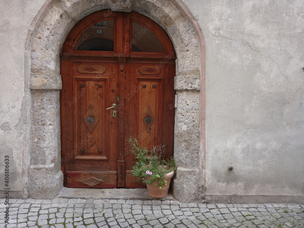Braune alte Türe in Mauerbogen mit Pflanzenkübel