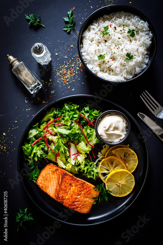 Fried salmon steak with mix of vegetables served on black plate on wooden table 