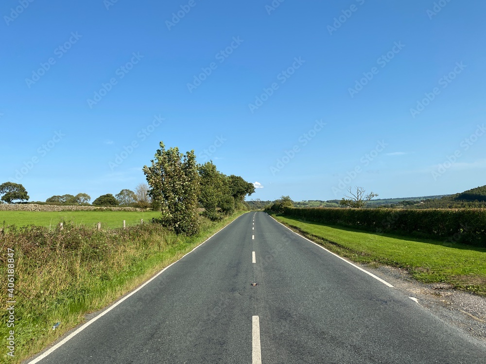 Looking along the, B6165, with trees and fields, set against a vivid blue sky in, Hartwith cum Winsley, Harrogate, UK