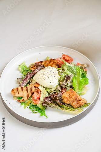 Caesar salad with croutons  quail eggs  cherry tomatoes and grilled chicken in white table
