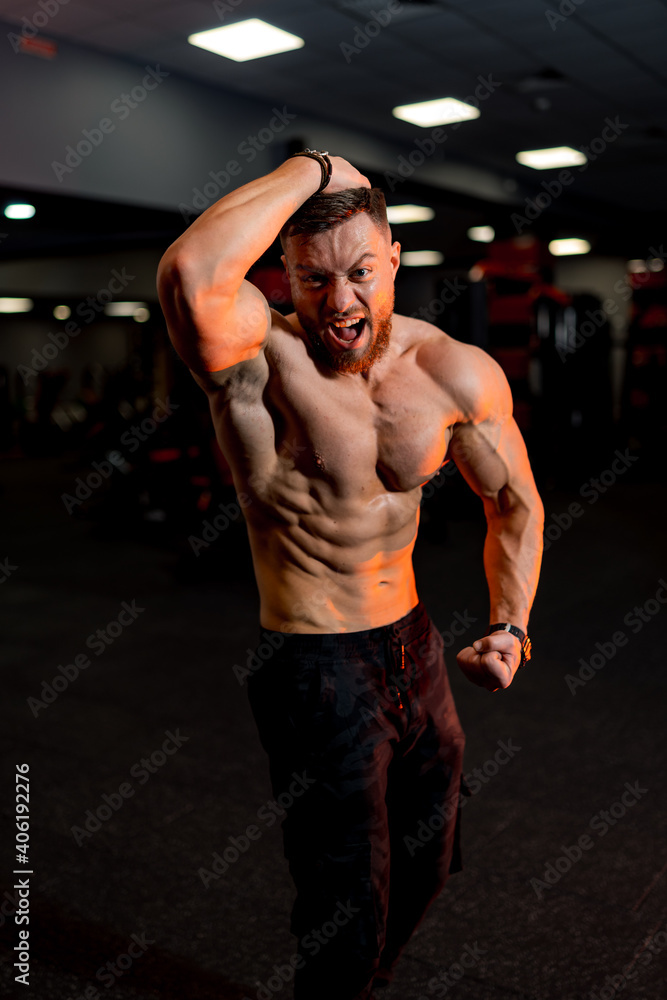 Fototapeta premium Attractive bodybuilder sportsman shows perfect body muscles on gym background. Fitness man. Bodybuilding and gym sport.