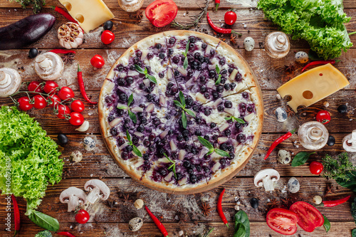 The pizza is surrounded by raw ingredients on the boards