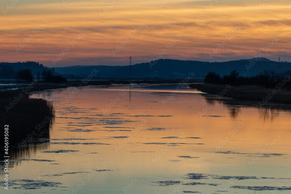Dusk at Gota river in western Sweden. Orange sky is reflecting in the calm water and ice sheets are floating in the river