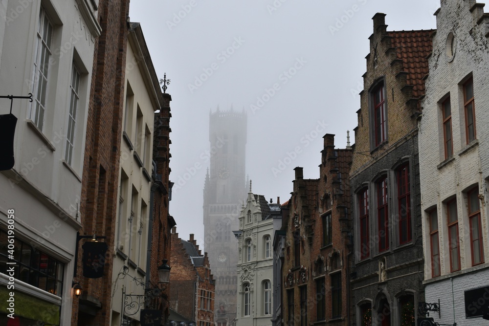 Medieval bell tower Belfry of Bruges in the fog and facade of other old buildings