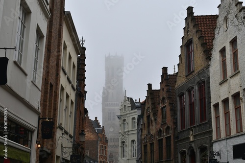 Medieval bell tower Belfry of Bruges in the fog and facade of other old buildings