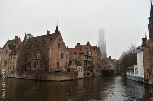 Famous picture spot in Brugge with the Belfry of Brugge in the background among fog © keremberk