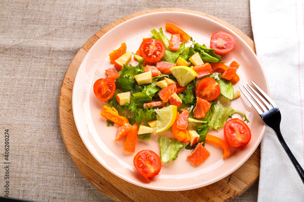 Salad with salmon and cherry tomatoes in a plate on a gray background on a wooden stand stand next to a fork and napkin. Salad with salmon and cherry tomatoes in a plate on a gray background on a wooden stand stand next to a fork and napkin.