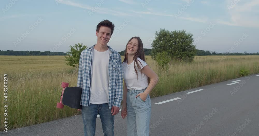 Couple looking at camera, girl poses and talks during a walk with skateboard Couple looking at camera, girl poses and talks during a walk with skateboard