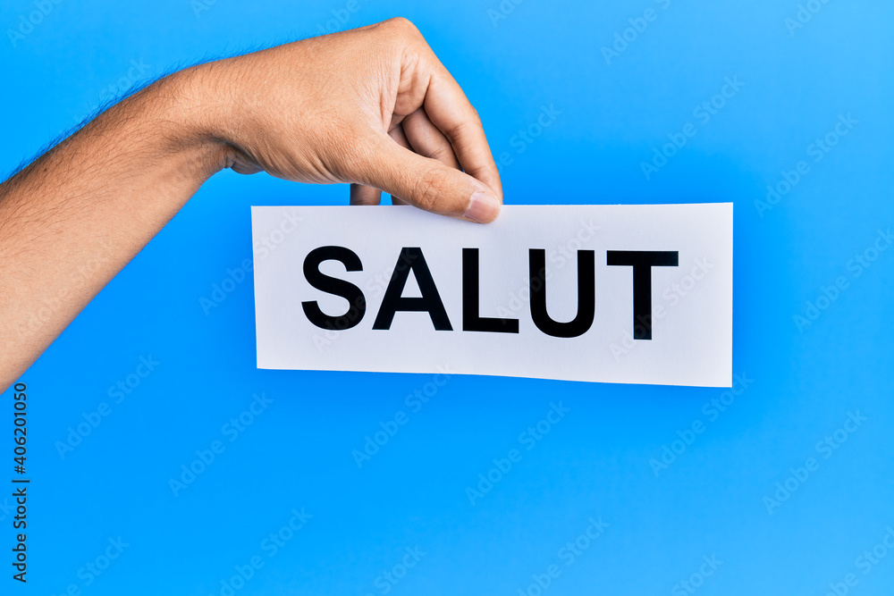 Hand of hispanic man holding salut word paper over isolated blue background. Hand of hispanic man holding salut word paper over isolated blue background.